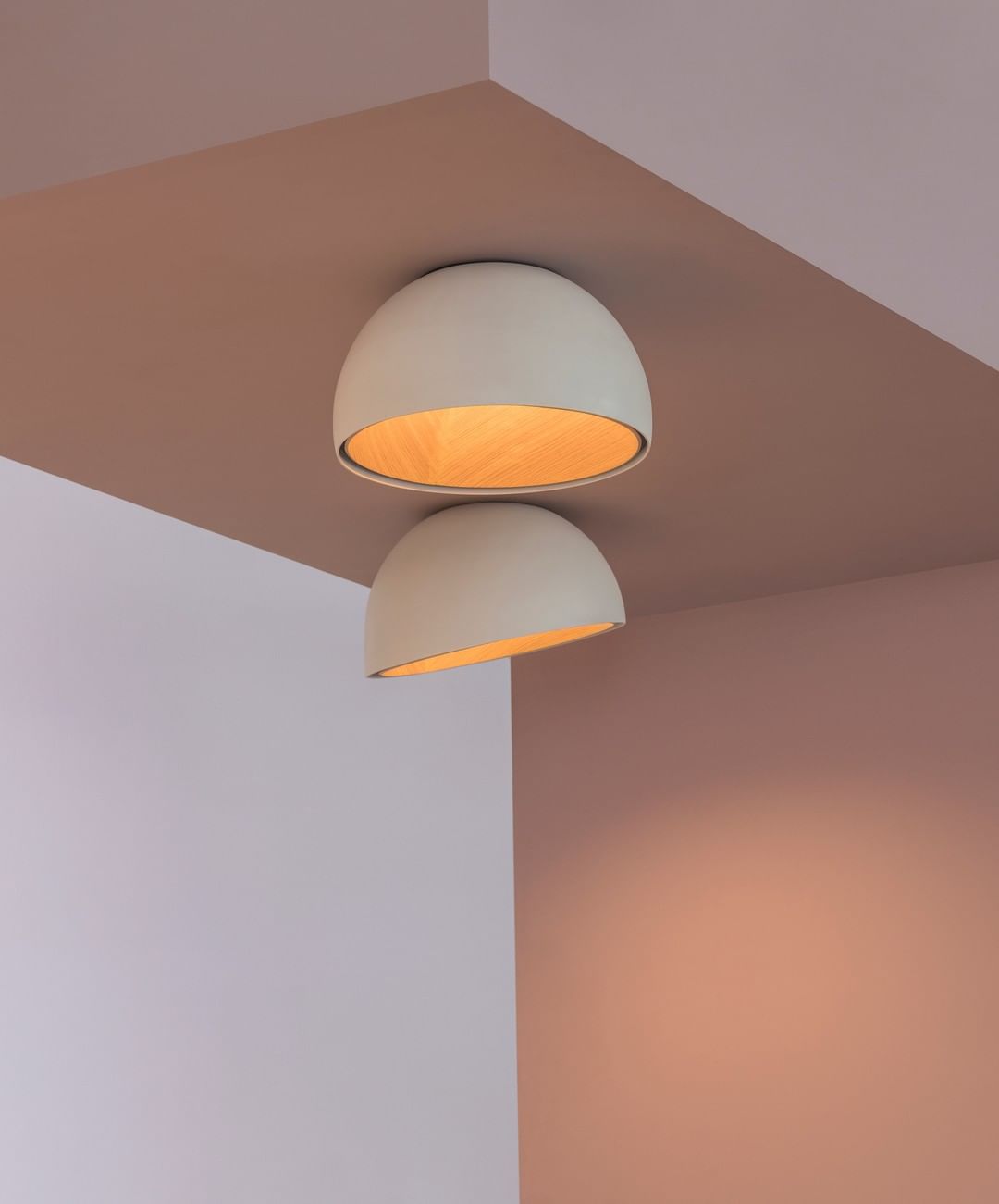 Two pale Clérachic dome ceiling lights, one above the other, in an angled corner with pink and lilac painted walls.