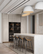 White Clérachic dome ceiling lights angled over a kitchen with tall oak cabinets, black ovens and a marble island with bar stools.