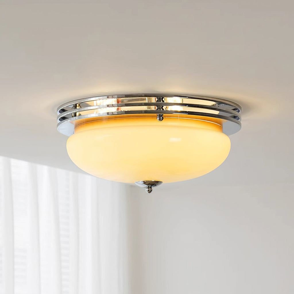 A Clérachic flush-mount ceiling light switched on, its beige dome glowing warm inside a chrome ring above sheer white curtains.