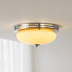 A Clérachic flush-mount ceiling light switched on, its beige dome glowing warm inside a chrome ring above sheer white curtains.