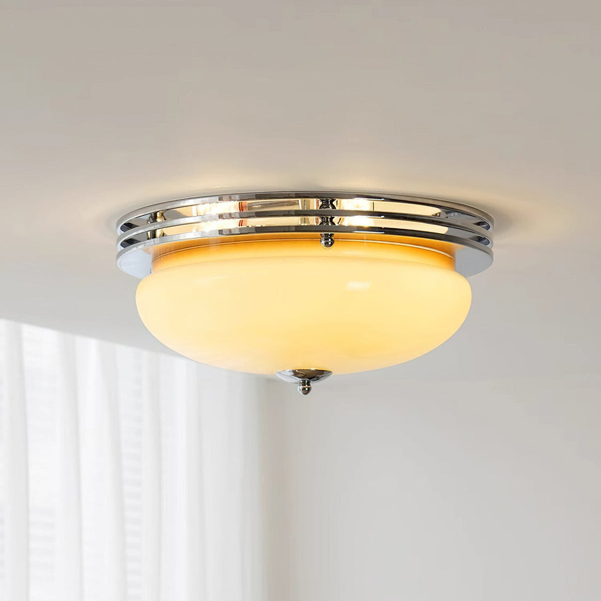 A Clérachic flush-mount ceiling light switched on, its beige dome glowing warm inside a chrome ring above sheer white curtains.