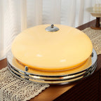 Same Clérachic dome light on the lace runner switched on, the beige glass glowing warm above its layered chrome rings.