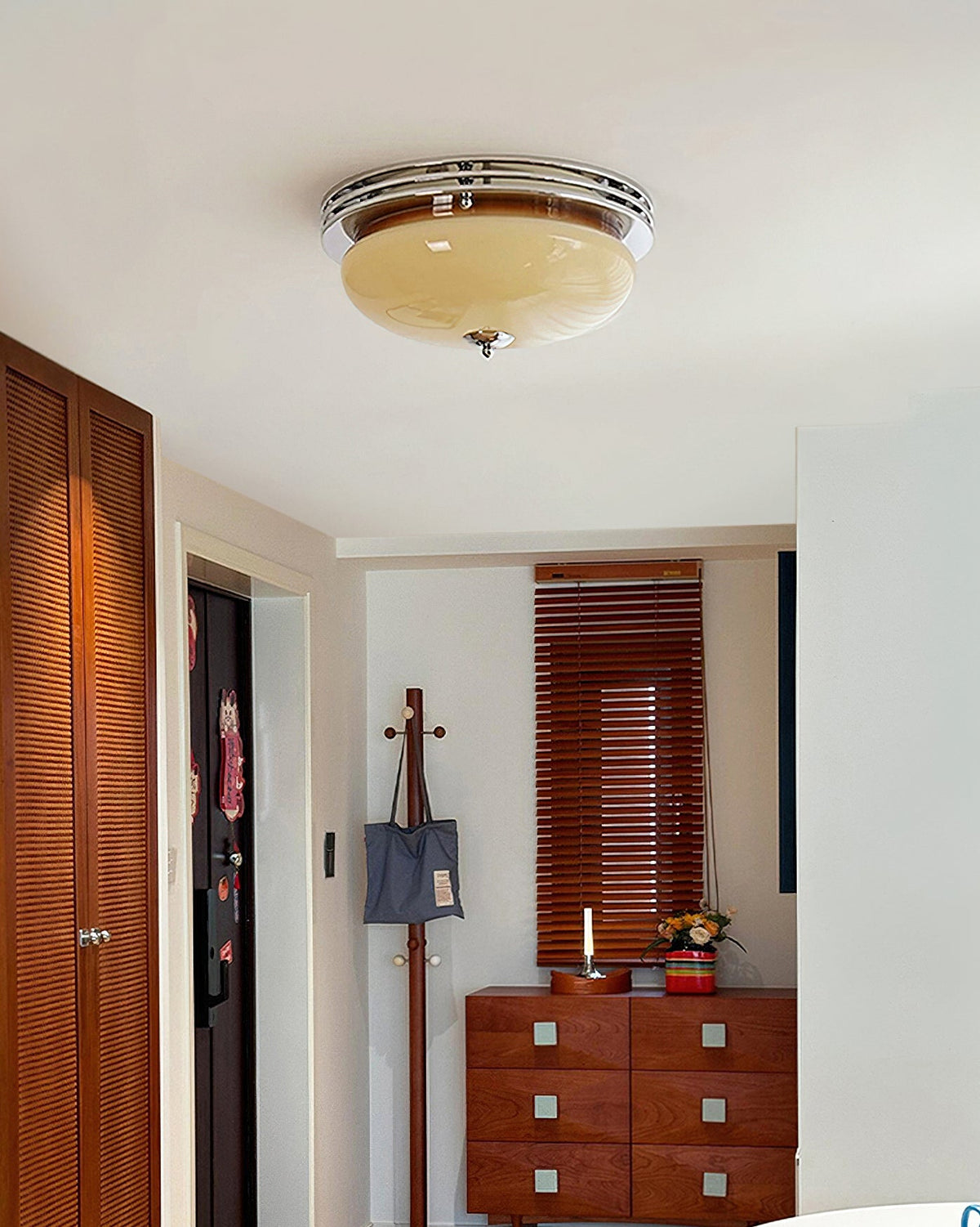 Clérachic flush-mount ceiling light seen from below in a narrow hall, with a wooden slatted door and a small chest of drawers beyond.