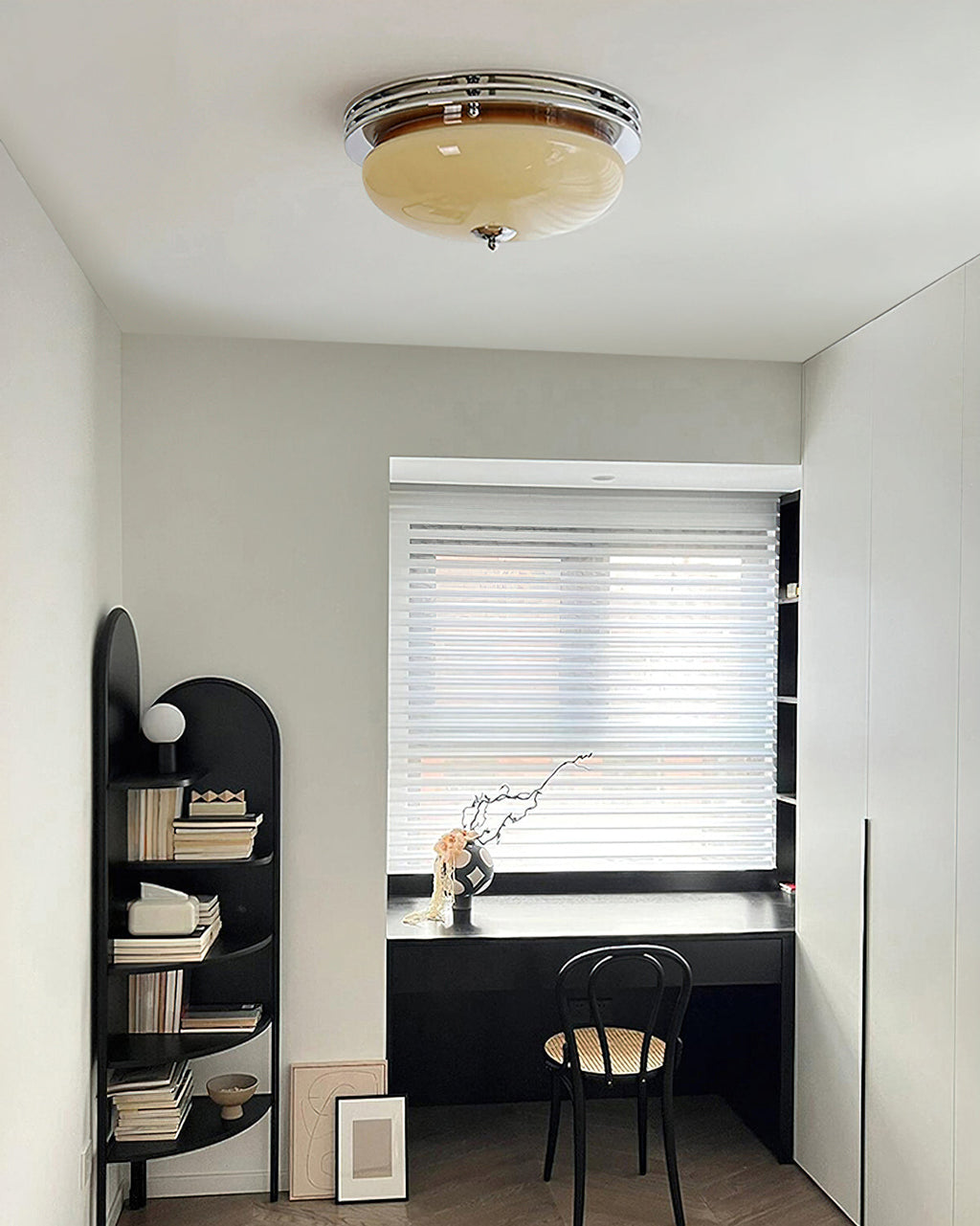 Small home-office alcove with a Clérachic dome ceiling light overhead, a black desk, arched shelving and a window with blinds.