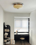 Small home-office alcove with a Clérachic dome ceiling light overhead, a black desk, arched shelving and a window with blinds.