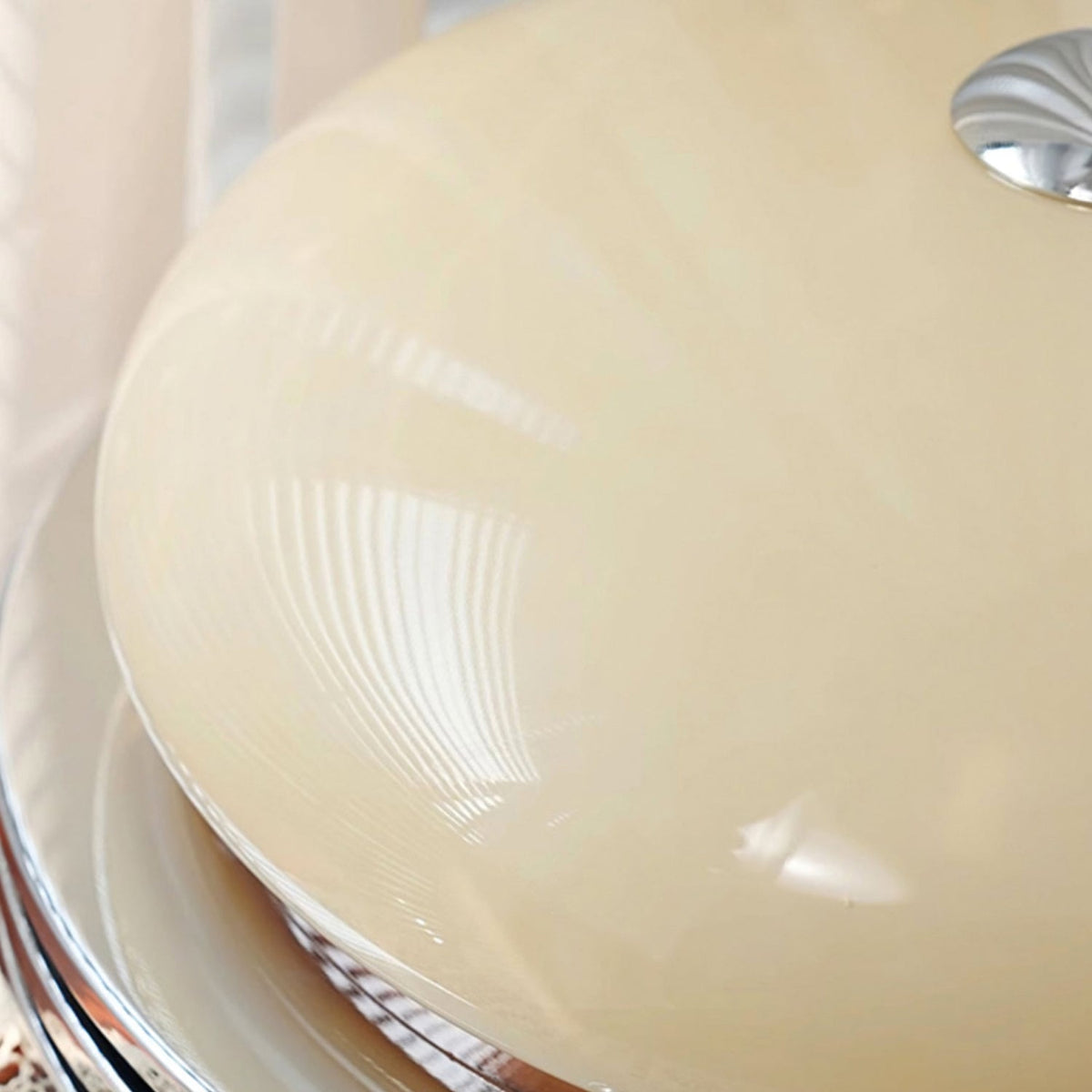 Close view of the smooth beige glass dome and chrome finial on this Clérachic ceiling light, with reflections across the surface.
