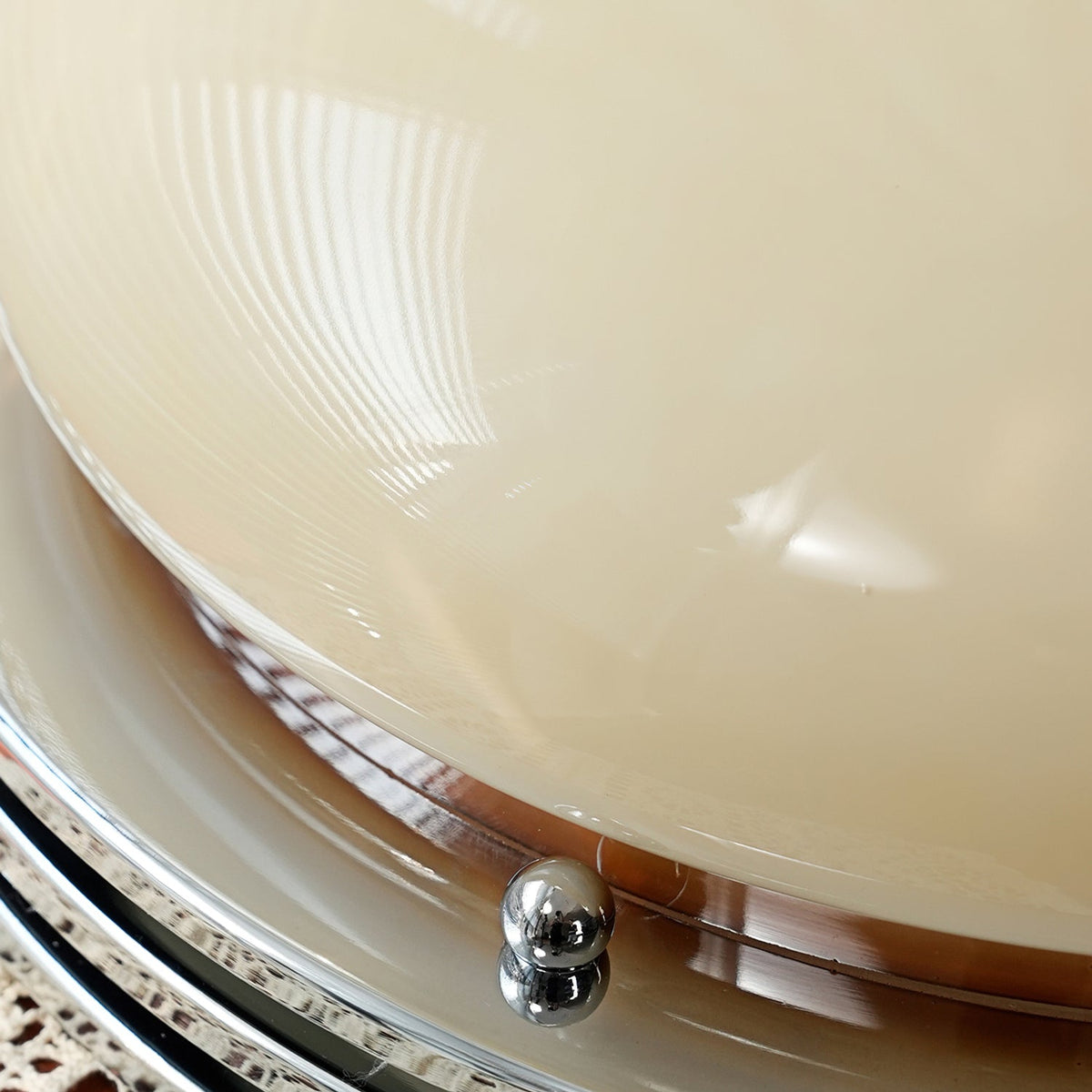 Close view of a chrome screw cap at the rim of this Clérachic dome light, with the beige glass and chrome rings behind it.