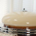 Low side view of this Clérachic ceiling light on a lace runner, showing the beige dome, chrome finial and stacked rings.