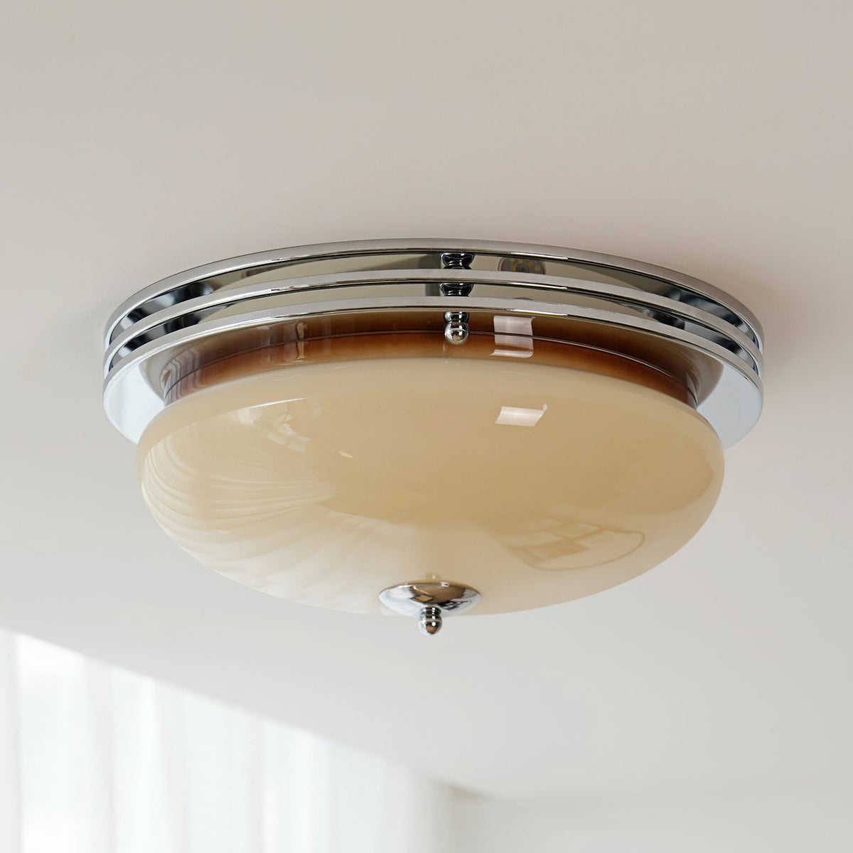 Underside view of a Clérachic flush-mount light fixed to a white ceiling, with a chrome ring and a beige glass bowl.