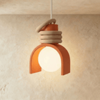 Clérachic pendant light in orange, lit, a terracotta arch shade around a glowing white orb with stacked sand-coloured rings