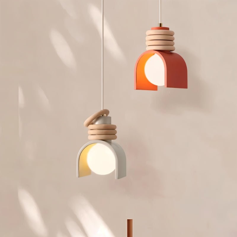 Clérachic pendant lights in white and orange hung at different heights against a soft blush wall with dappled light