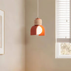 Clérachic pendant light in orange hanging in a corner of a cream room beside a window with white slatted blinds