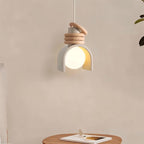 Clérachic pendant light in white hung above a round wooden side table and a book, its glowing orb framed by the arch