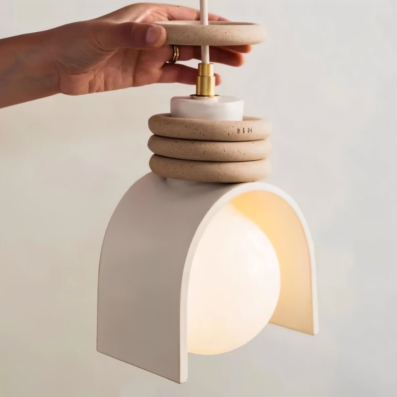 Clérachic pendant light in white held by hand, showing the brass cord grip, stacked speckled rings and the arch shade