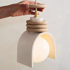 Clérachic pendant light in white held by hand, showing the brass cord grip, stacked speckled rings and the arch shade