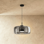 Clérachic wide smoked glass dome pendant on a slim black cord, lit from within, against a limewash wall.