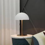 White dome lamp from Clérachic on a round brass base, on a marble side table next to soft white curtains.