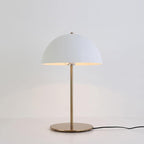 Lit white dome table lamp from Clérachic on a pale backdrop, with its black cord trailing from the brass base.