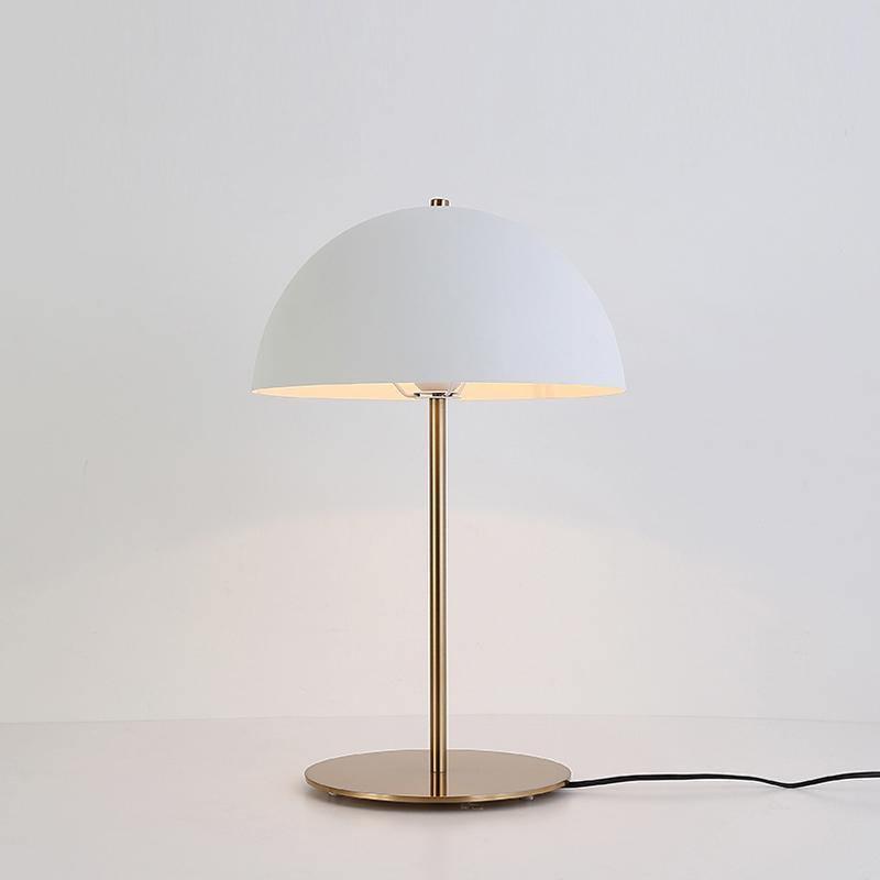 Lit white dome table lamp from Clérachic on a pale backdrop, with its black cord trailing from the brass base.