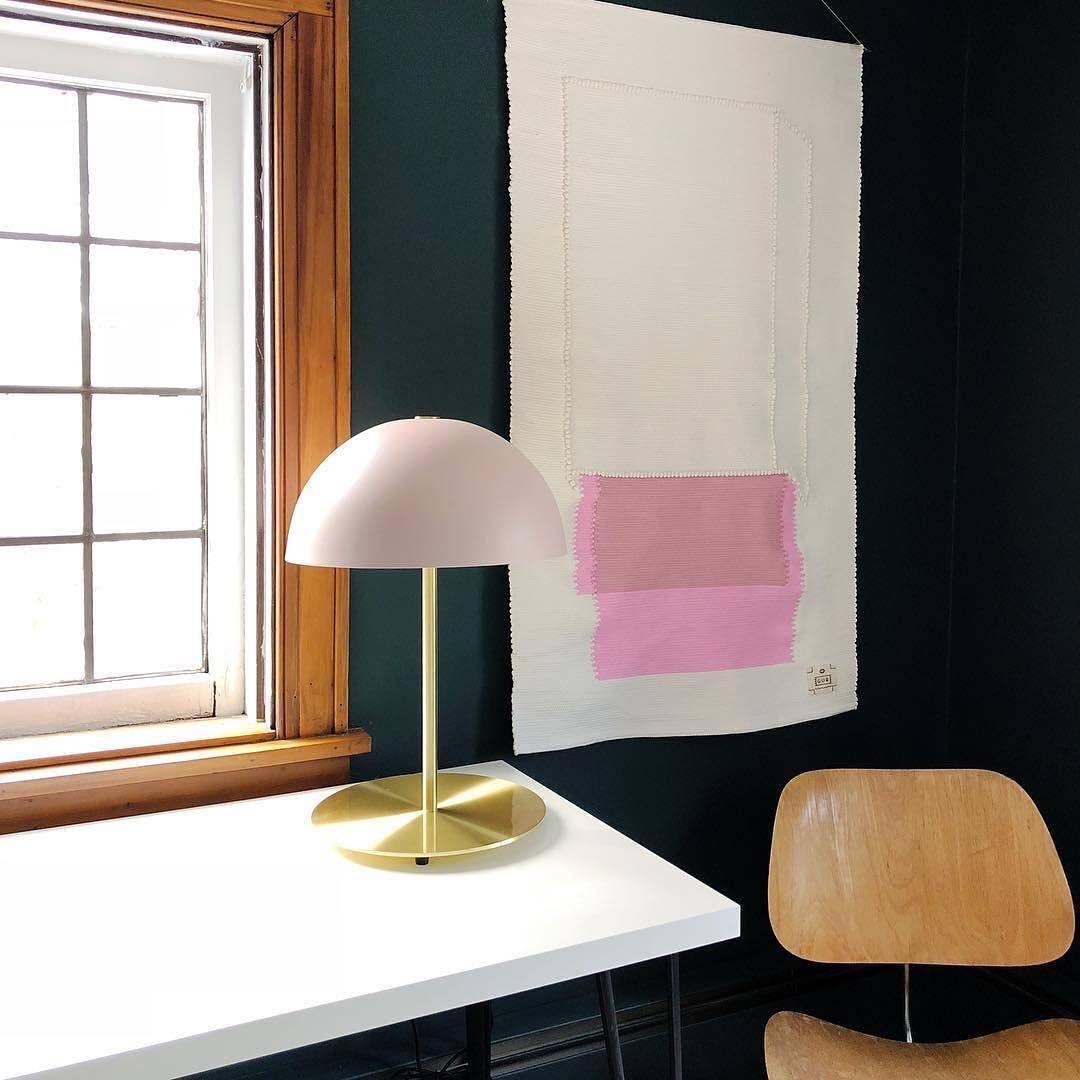 A pink dome lamp from Clérachic on a white desk by a window, with a pink-and-white wall hanging behind it.