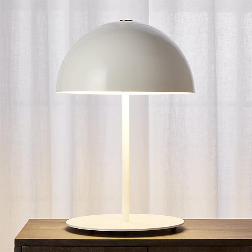 Close view of a white dome table lamp from Clérachic with a white stem and base, on a wooden table before sheer curtains.