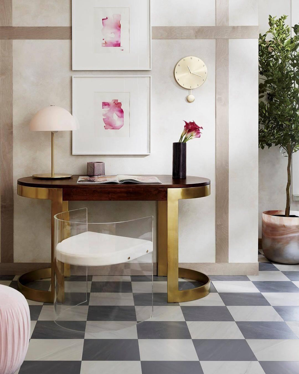 Pink dome table lamp from Clérachic on a curved wooden console with a clear acrylic chair and framed pink prints.