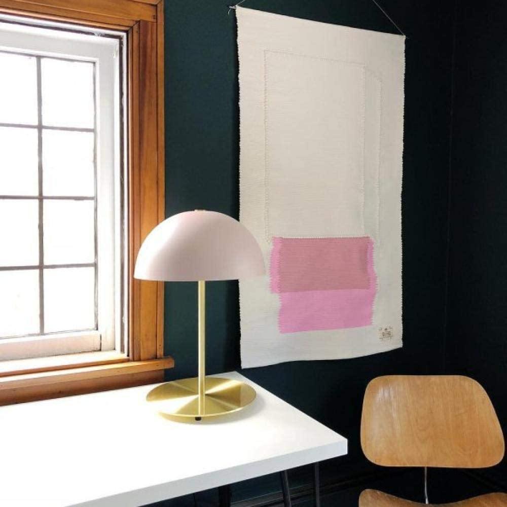 This Clérachic table lamp with a pale pink dome shade on a white desk by a paned window, with a wall hanging behind.