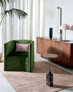 Wide room view with a pink Clérachic dome lamp on a sideboard behind a green velvet chair and a pink rug.