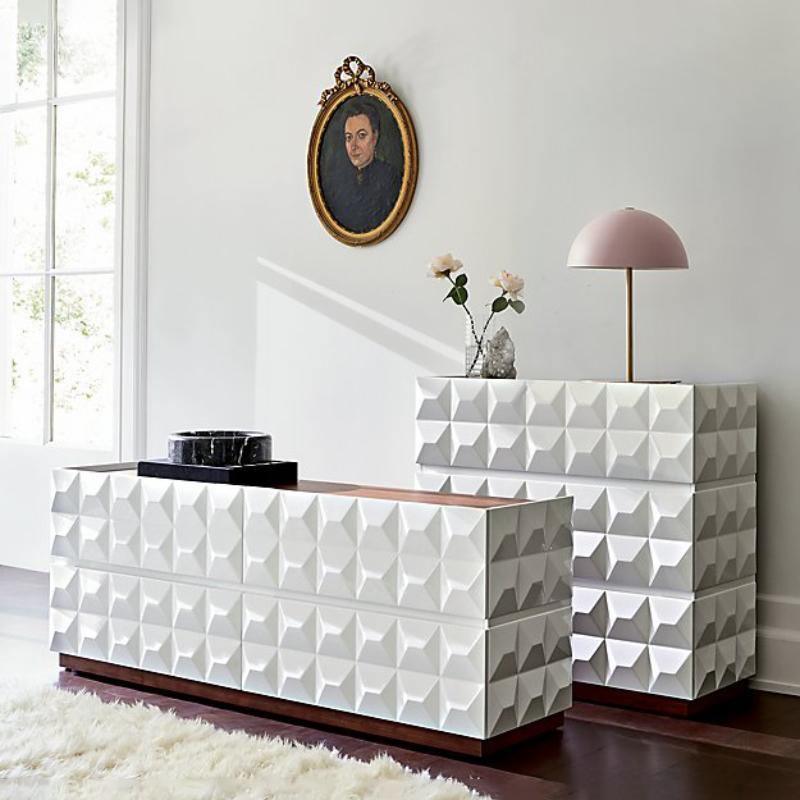 A pink-shaded Clérachic table lamp on a white geometric-panelled chest of drawers, under a framed portrait.