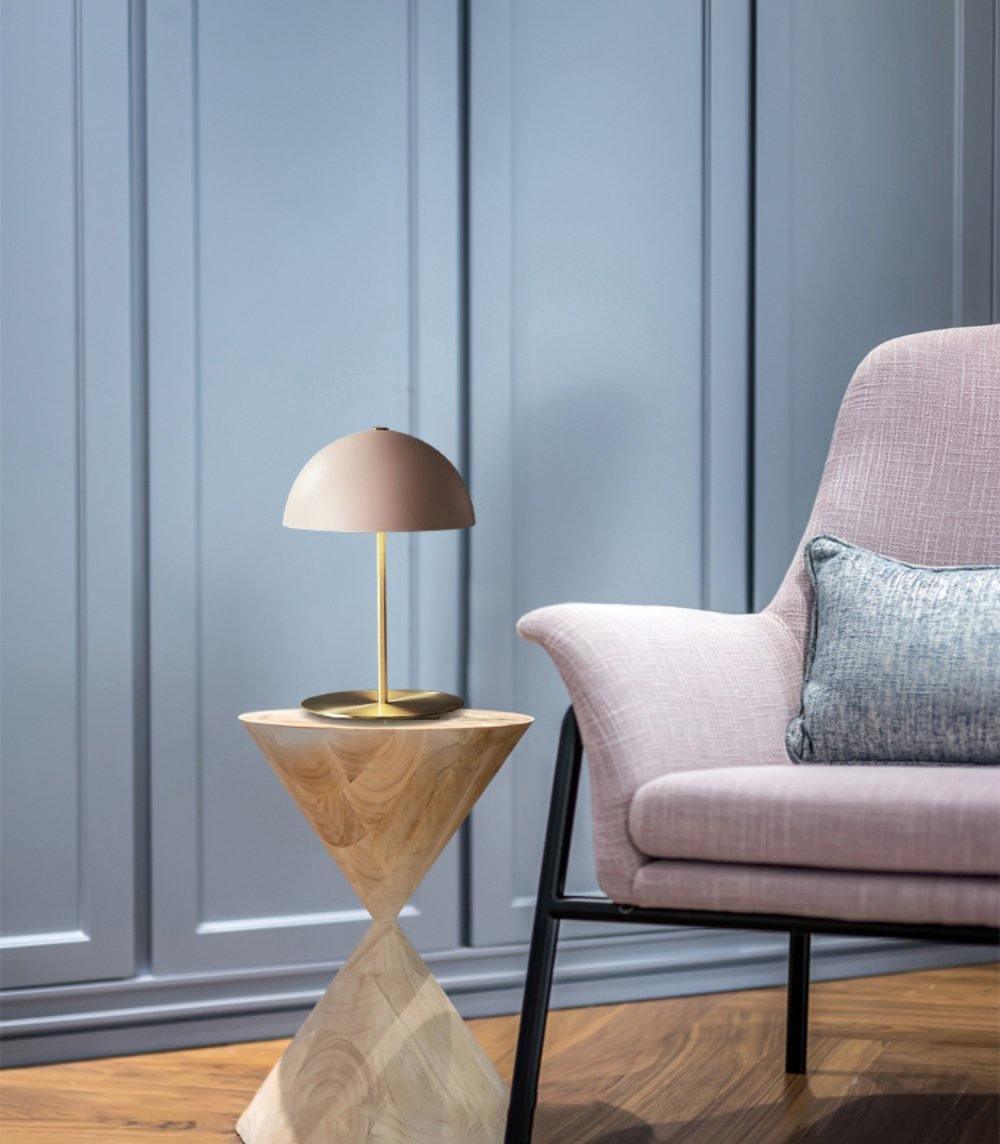 Small Clérachic table lamp with a muted pink dome, on a carved wooden side table beside a pink armchair.