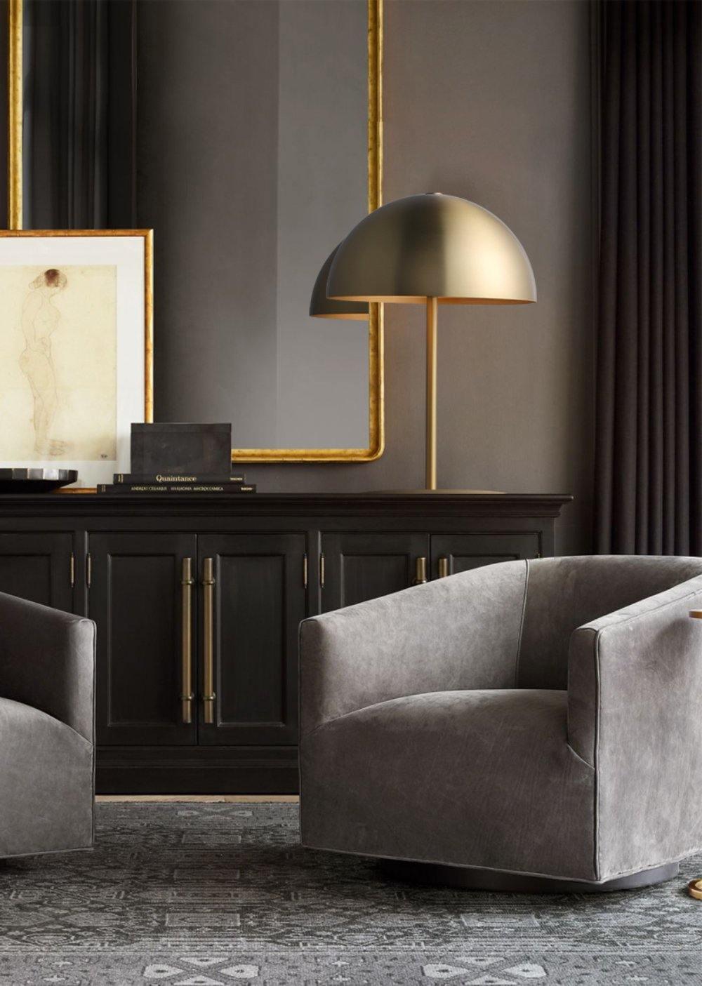 Brass dome table lamp from Clérachic on a dark sideboard, in a moody room with grey armchairs and a gilt mirror.