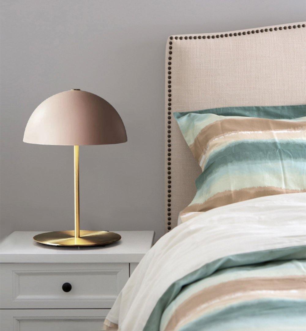 Pink dome lamp from Clérachic on a white bedside table with a drawer, next to a bed in striped teal and sand linen.