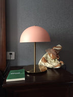 Coral-pink dome table lamp from Clérachic on a dark wooden table, beside a green book and a small soft toy.