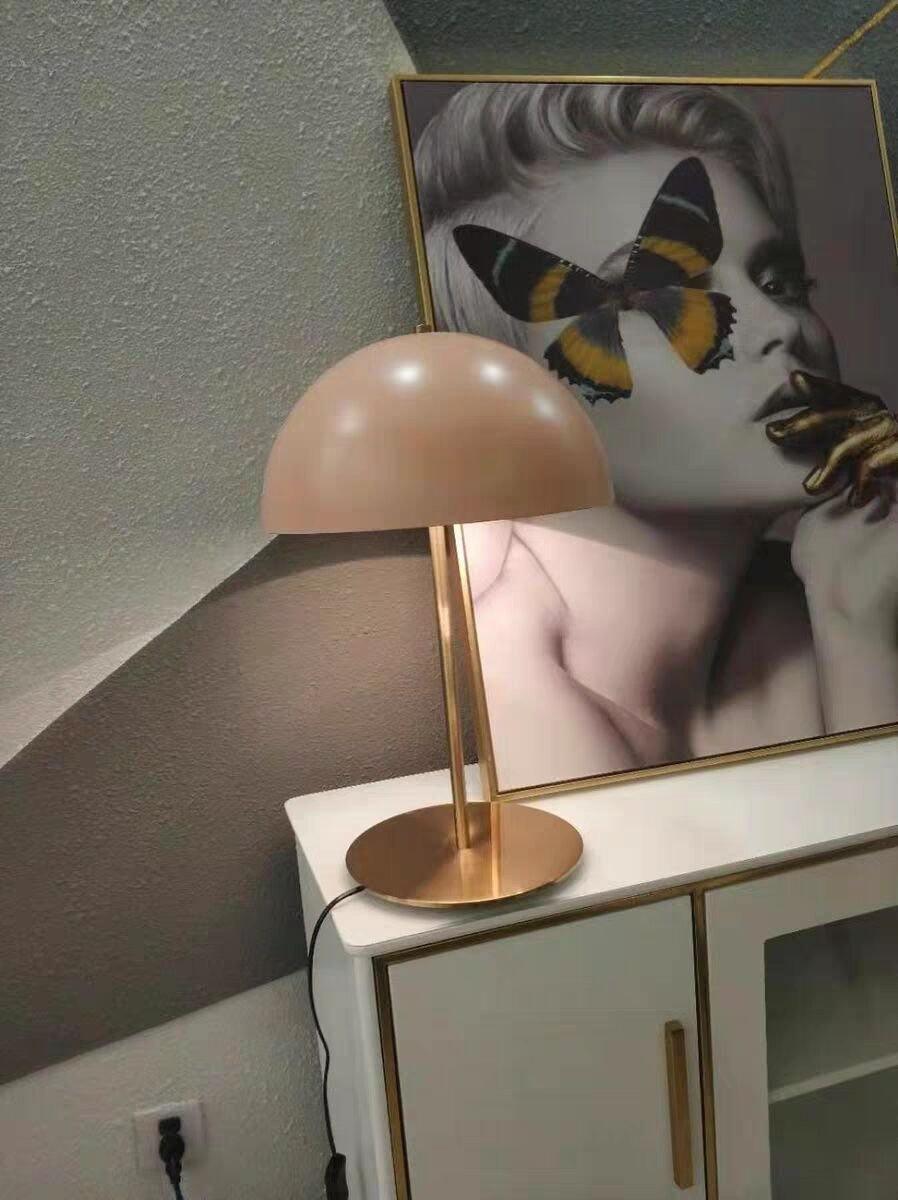 Pink dome Clérachic table lamp on a white cabinet, in front of a framed butterfly artwork on a green-grey wall.