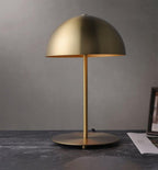 Brass-gold dome table lamp from Clérachic on a dark desk, set against a plain grey wall with papers at one side.