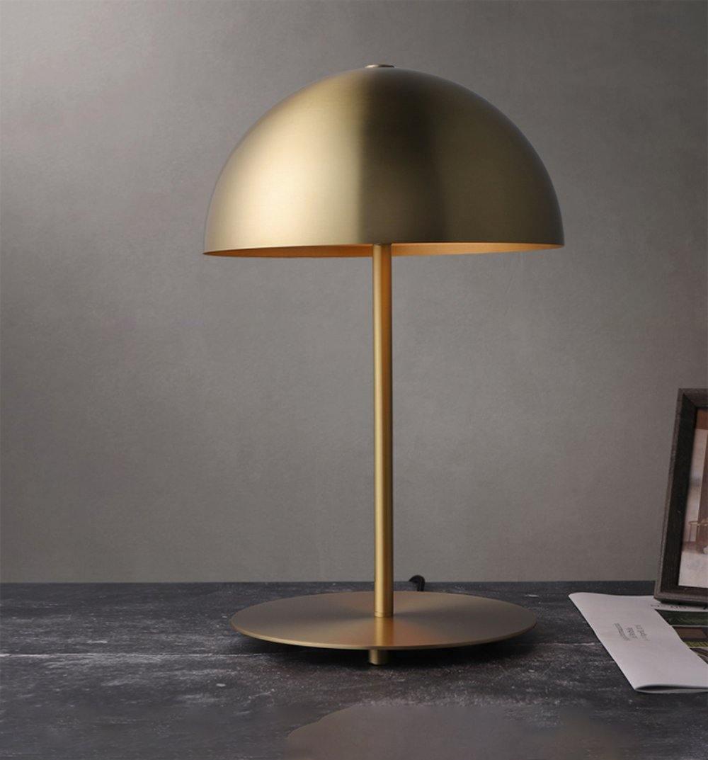 Brass-gold dome table lamp from Clérachic on a dark desk, set against a plain grey wall with papers at one side.