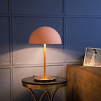 Pink dome table lamp from Clérachic on a round black marble table, in front of blue wall panelling and a magazine.