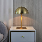 Gold dome table lamp from Clérachic on a white bedside chest, against a ribbed grey wall and a curved chair.