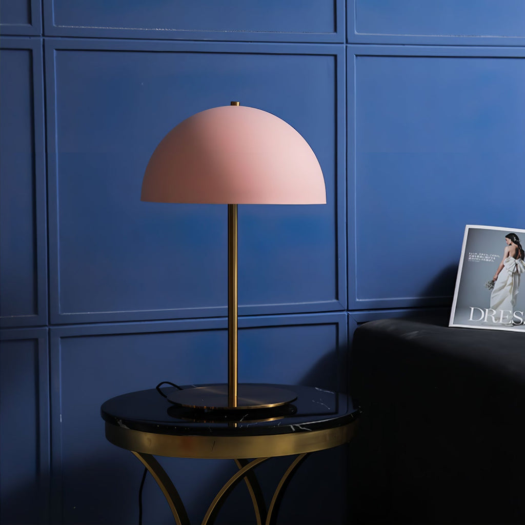 Pink dome lamp from Clérachic on a black marble side table with a brass frame, against blue panelled walls.