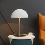 A white Clérachic dome table lamp beside a cup and saucer on a marble stool, with an orange armchair at the edge.