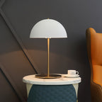 Wide view of a white dome lamp from Clérachic on a marble and teal quilted stool, with a cup and an orange chair.