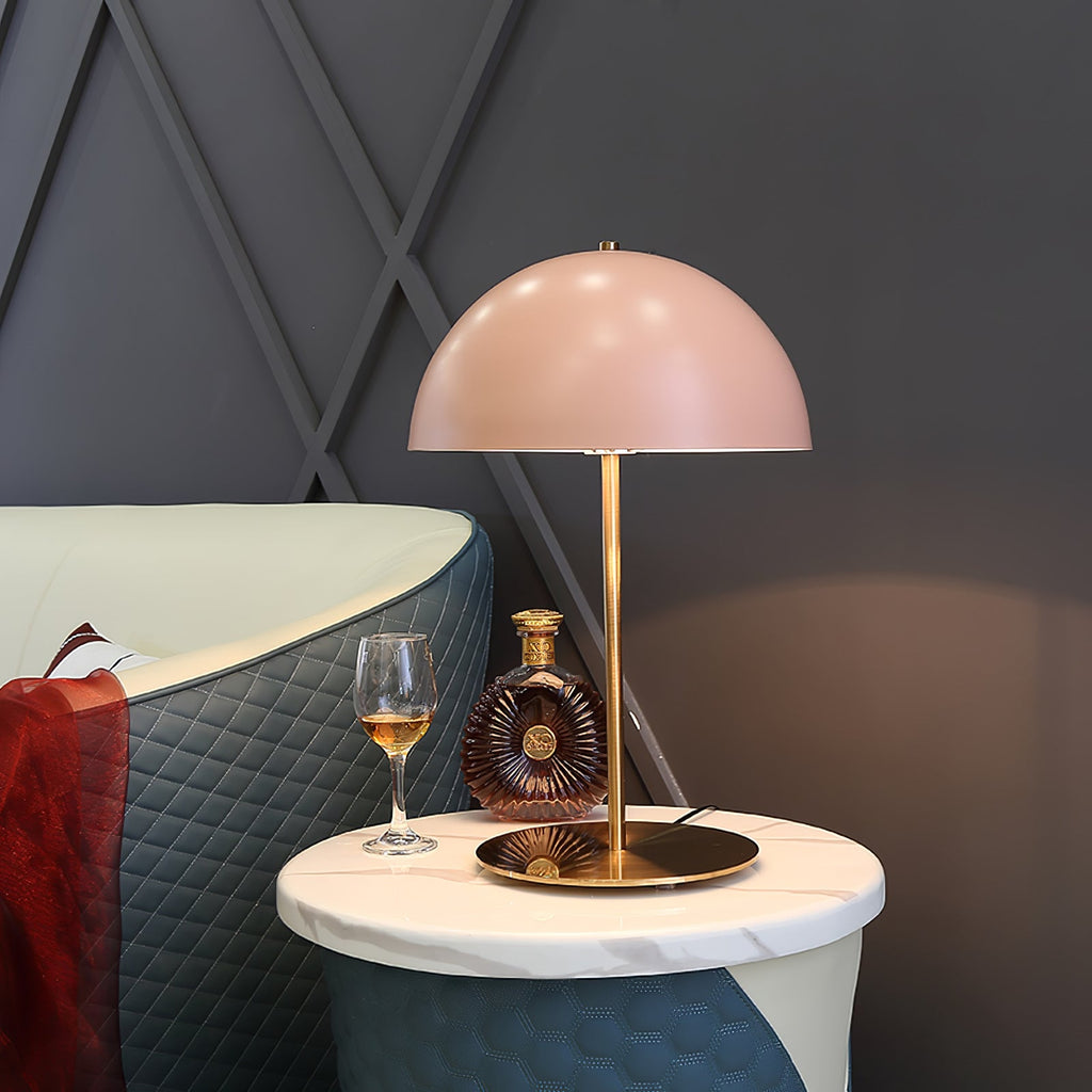 This Clérachic table lamp with a pink dome sits on a marble side table next to a wine glass and a decanter.
