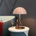 Pink dome table lamp from Clérachic on a round marble table, beside a glass of amber drink and a cut-glass decanter.