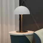 A white dome table lamp from Clérachic on a marble stool in front of cream curtains and a dark geometric wall.