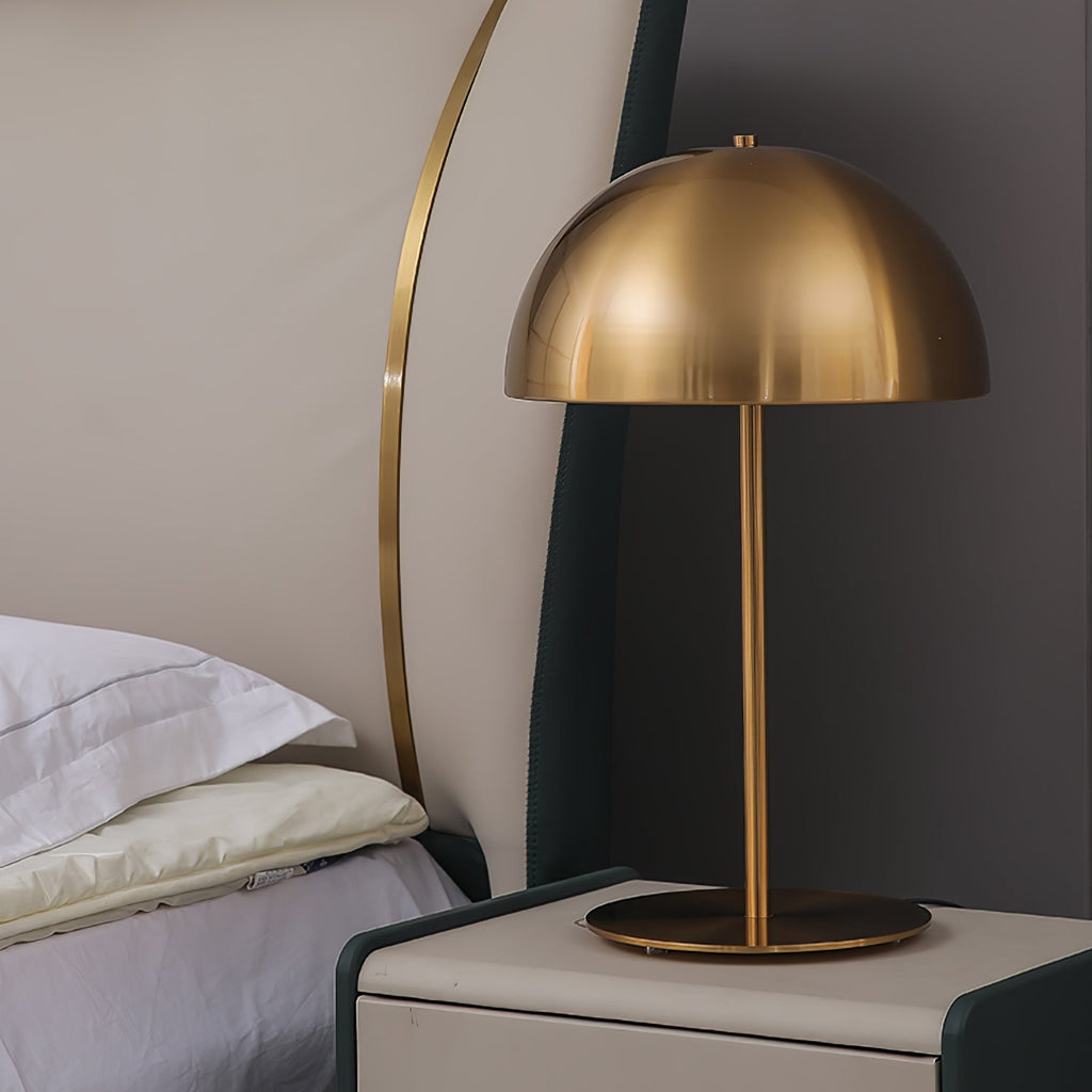 Gold dome table lamp from Clérachic with a brushed brass shade, on a white bedside cabinet beside a bed.