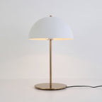 Lit white dome table lamp from Clérachic on a pale surface, with a black cord and a plain light-grey backdrop.