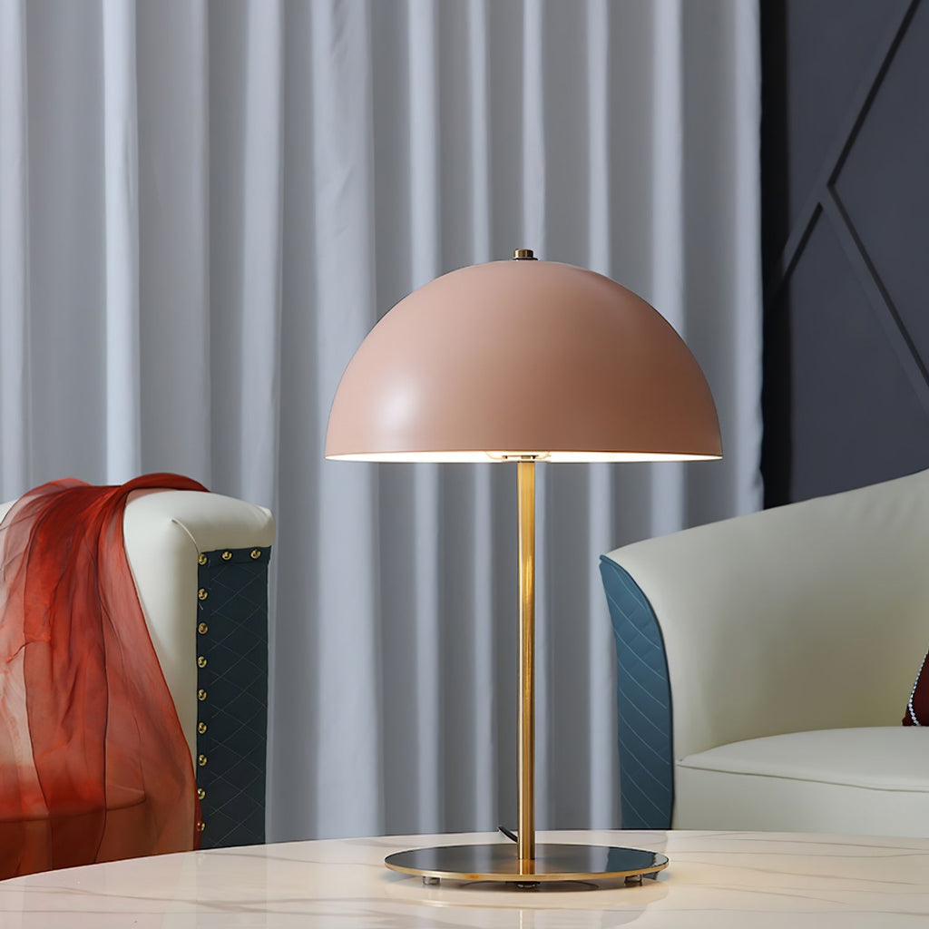 Close view of a pink dome table lamp from Clérachic on a marble table, with a cream sofa and a red throw behind.