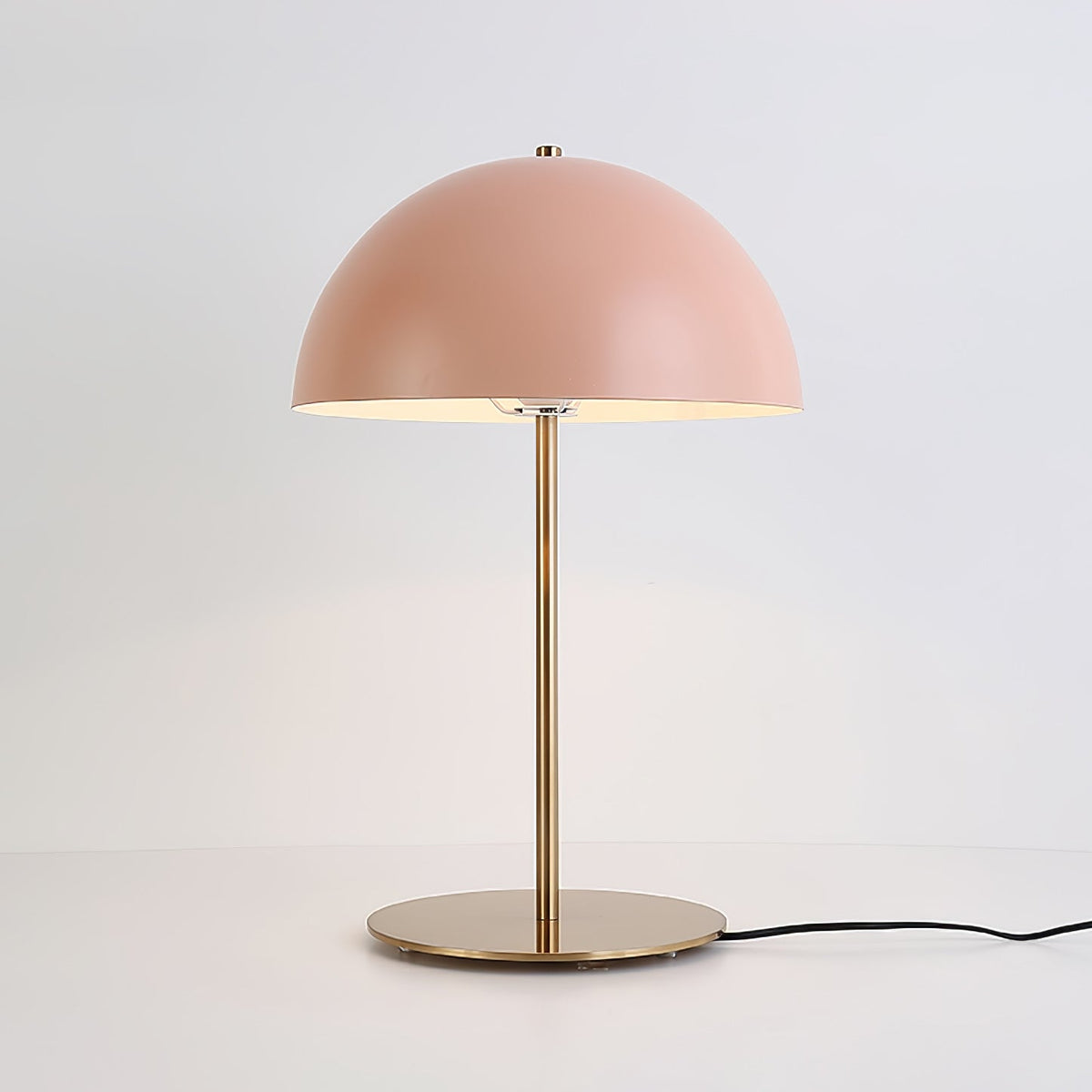 Lit pink dome table lamp from Clérachic on a light-grey backdrop, with a black cord running from its brass base.