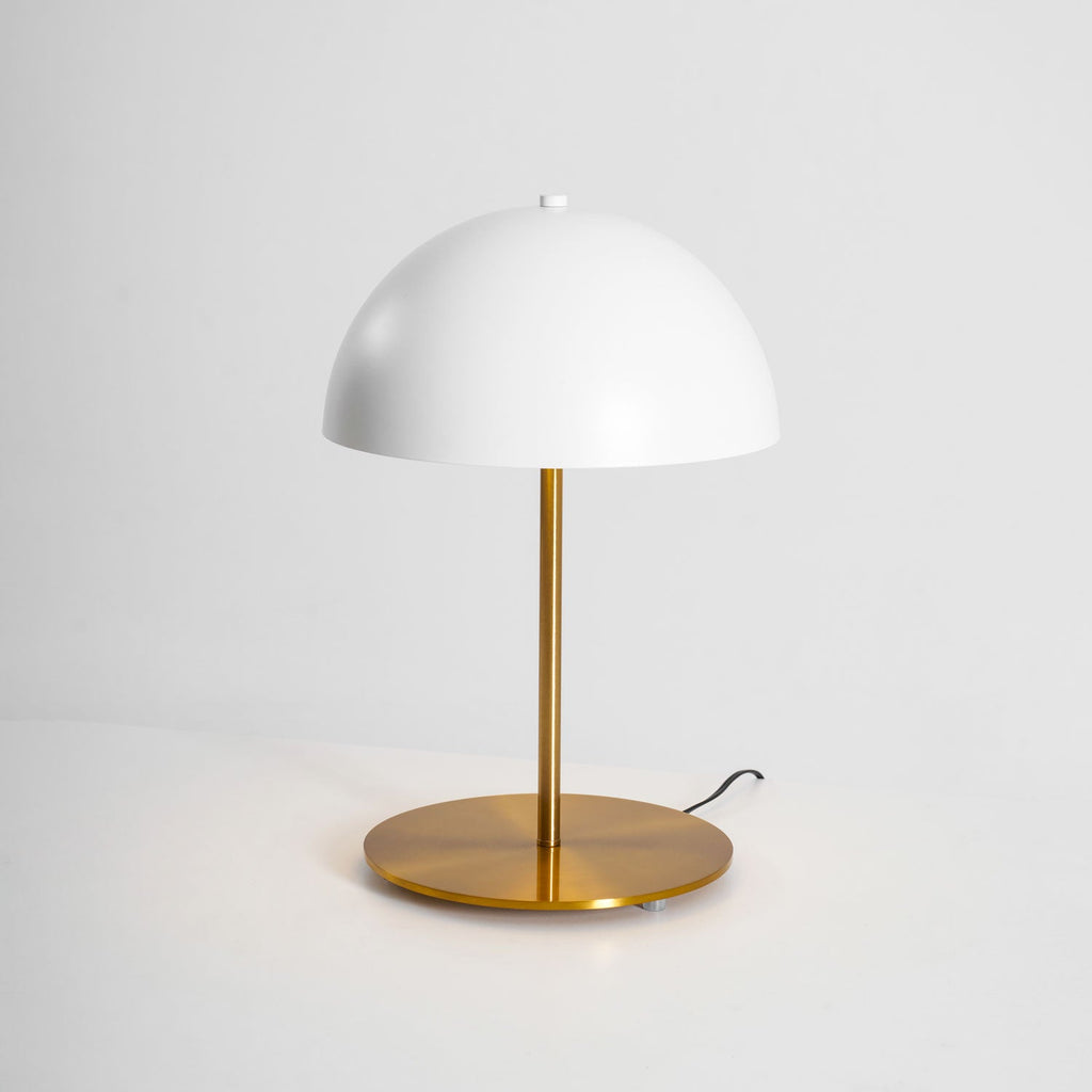 White dome table lamp from Clérachic with a brass base and a short black cord, on a pale grey backdrop.