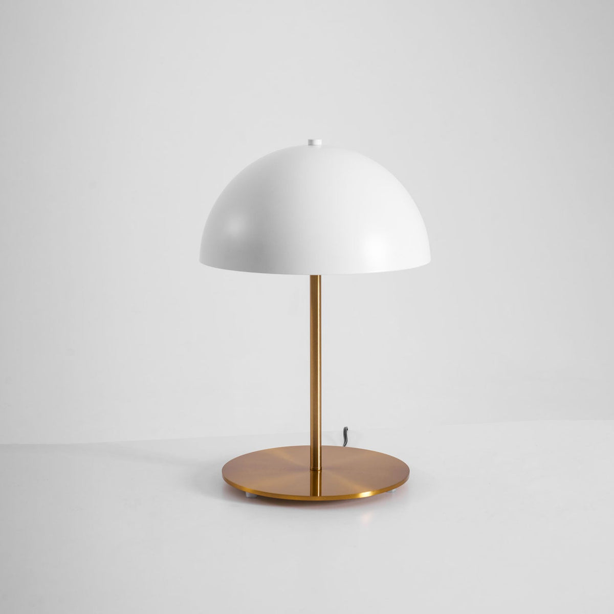 Angled view of a white dome table lamp from Clérachic with a copper-toned brass base, on a pale studio background.